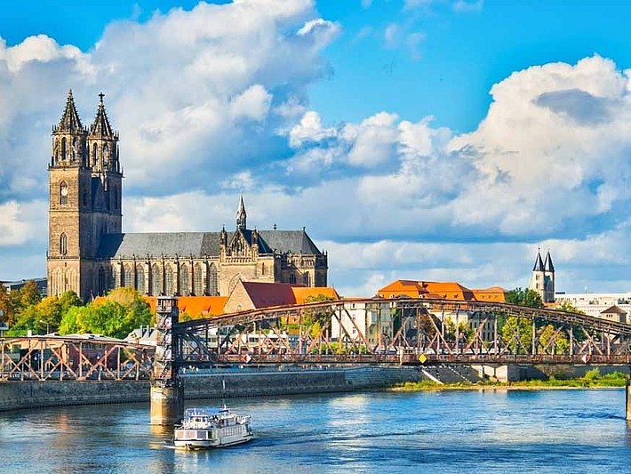 Die Magdeburger Kathedrale vor blauem Himmel mit der Elbe und einer Brücke im Vordergrund