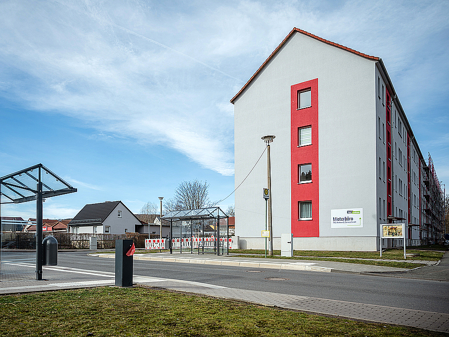 Modernes Wohngebäude mit markanten roten Fassadenakzenten und einer Bushaltestelle direkt vor der Tür