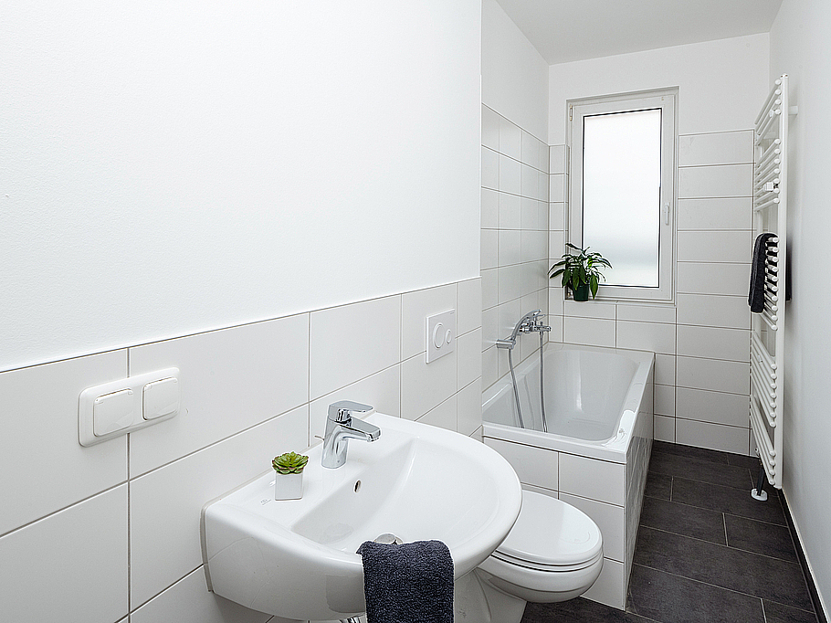 Schick saniertes Badezimmer mit weißen Wandfliesen und dunklen Bodenfliesen mit Badewanne, Handtuchheizkörper und WC in der Feldstraße in Stadtilm